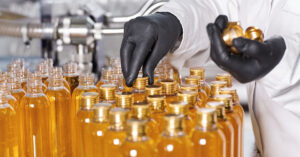Laboratory scientist in black rubber gloves screwing caps of transparent plastic bottles filled with shampoo