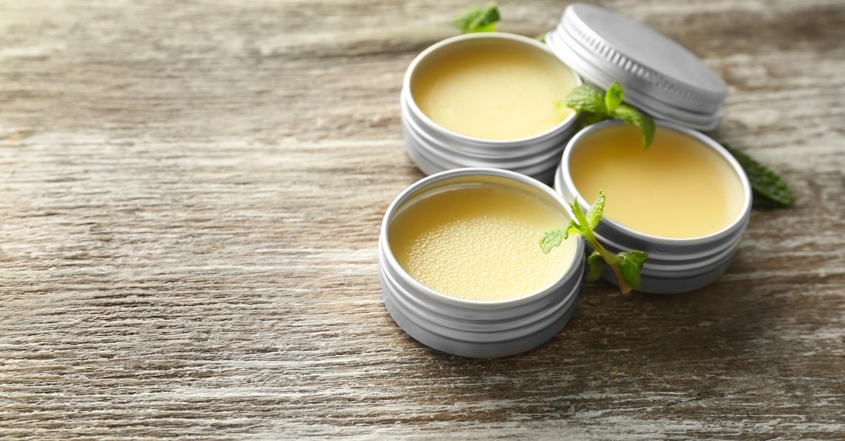 Tins of lip balm salve with mint leaves on a wooden surface